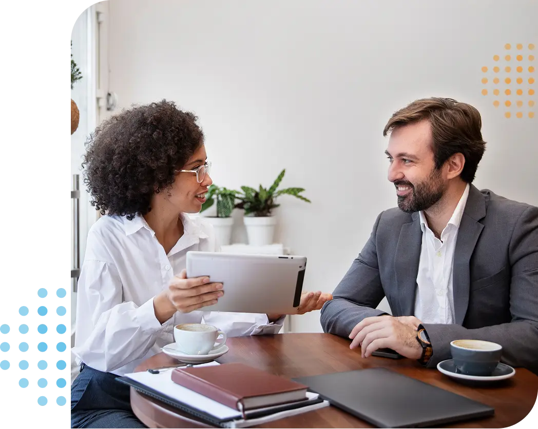 businesswoman & businessman smiling & talking while sat at a table