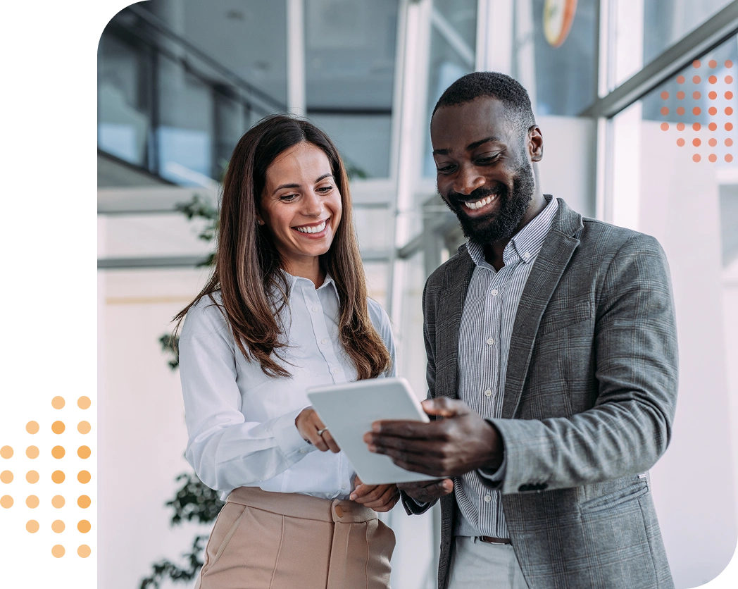 businessman & businesswoman standing & looking at a tablet while smiling