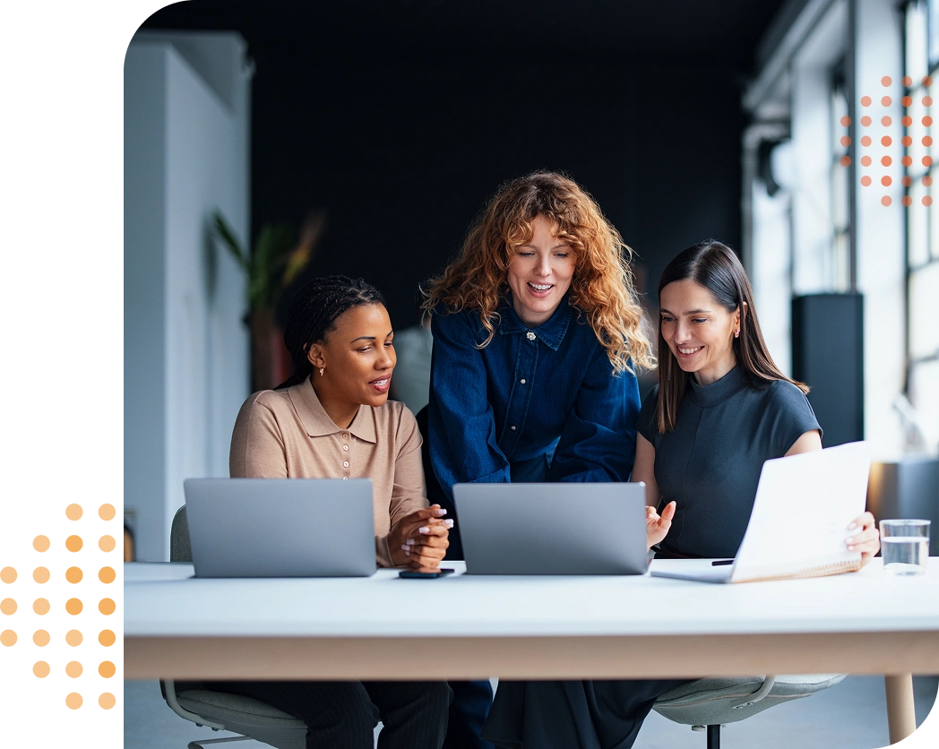 three businesswomen smiling & looking at their laptops sat side by side on the table